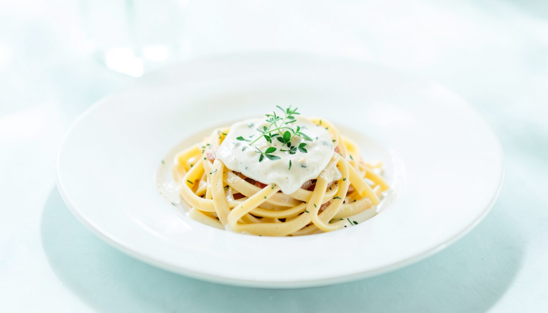 Bright, airy photograph of a beautifully plated pasta dish with delicate herbs and a soft cream sauce on white ceramic